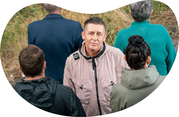 A photo taken from an aerial view looking down towards a man in a coat looking up. He has two people in front of him and two people behind him but they are all facing the opposite way to him.
