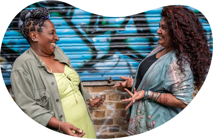 A photo of two women laughing together in front of a wall of graffiti
