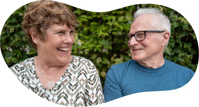 A close up photo of a woman and man sitting on a park bench smiling at each other