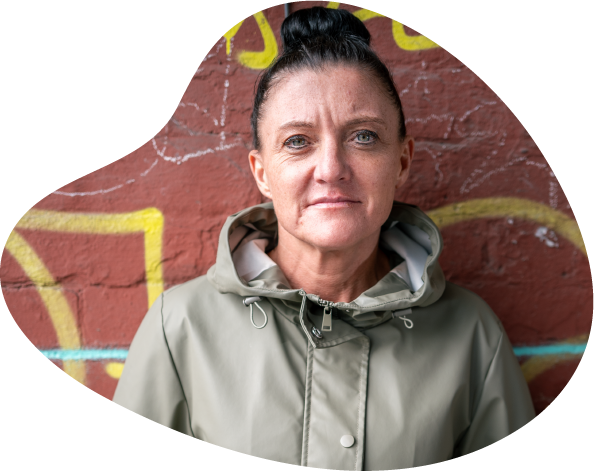 A photo of a women wearing a green raincoat looking pensive in front of a brick wall