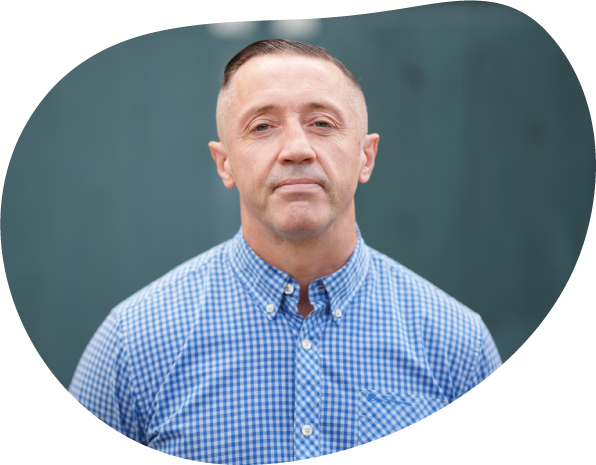 A photograph of Steven, a volunteer at Waythrough's Reconnect service. He is looking straight at the camera and wearing a blue and white checked shirt.